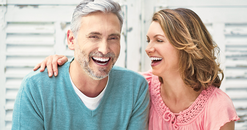 Husband and wife smile and laugh because they have benefitted from dental implants