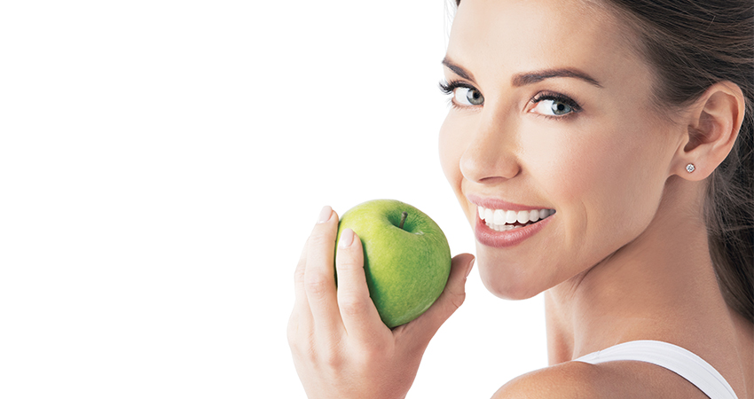 Woman with dental veneers holds a granny smith apple
